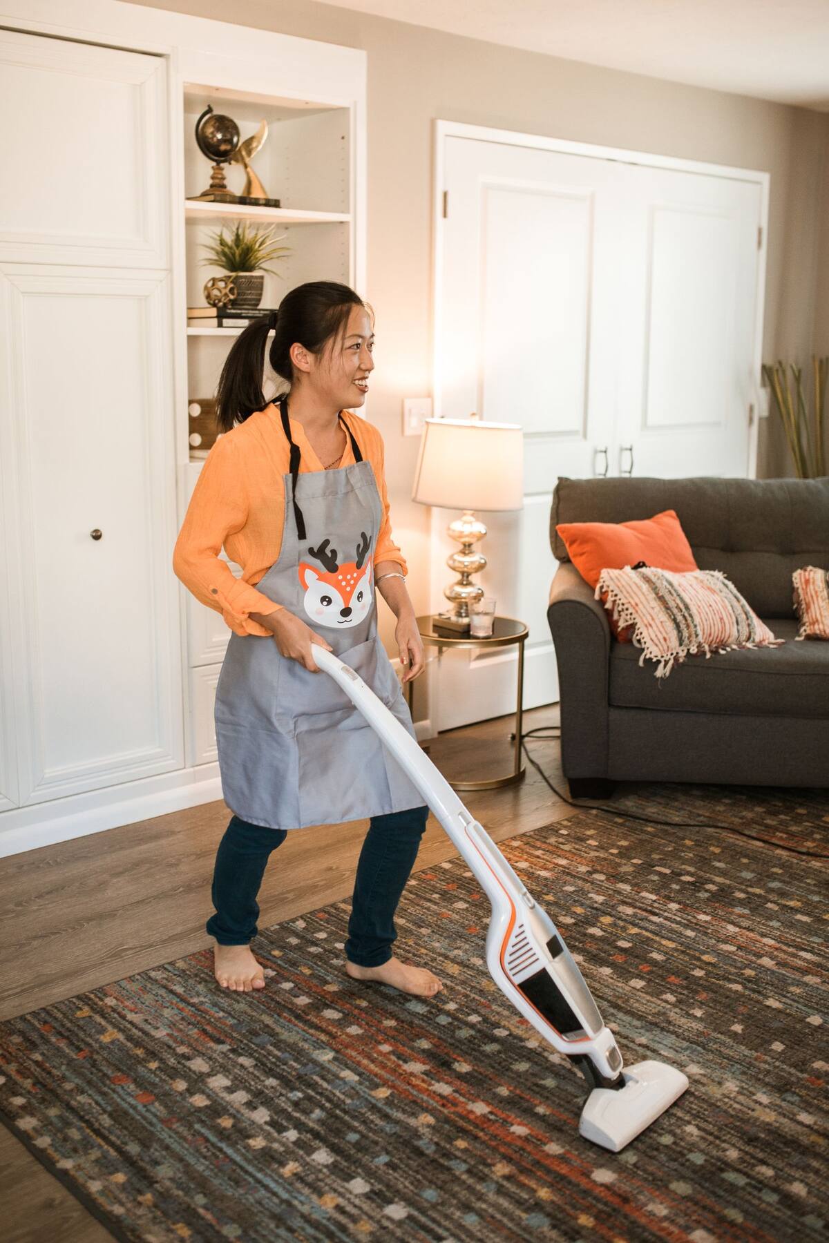 Woman vacuuming a living-room area rug with a stick vacuum.